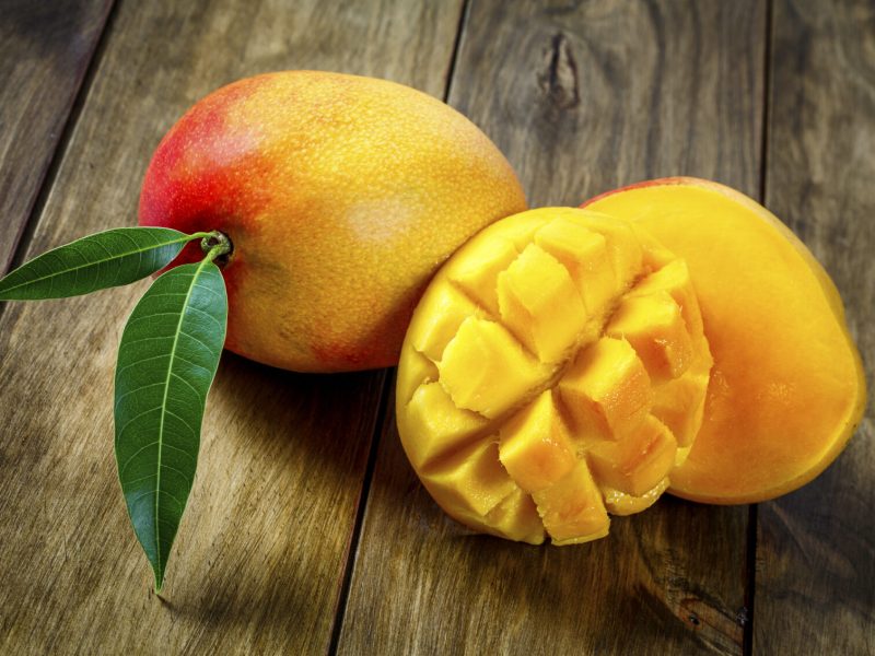 Tropical fruits - Sliced mango on a wooden table. The mango belongs to the genus Mangifera and to the flowering plant family Anacardiaceae.  The mango is a juicy stone fruit and is native to south and southeast Asia, and now available all over the world. Consisting of numerous tropical fruiting trees and with many varieties it is cultivated mostly for edible fruit. The majority of these species are found in nature as wild mangoes, nevertheless, in South America there are many big plantations for commercial purposes. The mango with the banana has become two of the most cultivated fruits in the tropics